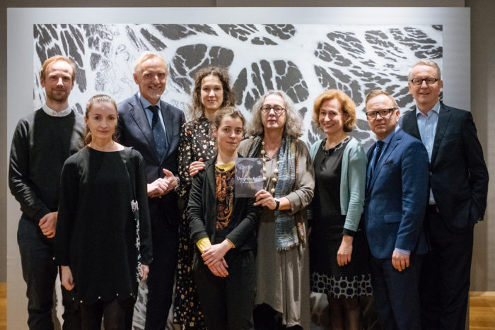 Zehn Personen posieren vor einem vom Großen Bruch inspirierten abstrakten Schwarz-Weiß-Kunstwerk.
