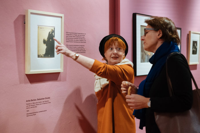 Zwei Frauen diskutieren über das Kunstwerk Der große Bruch in einer Galerie mit rosa Wänden.