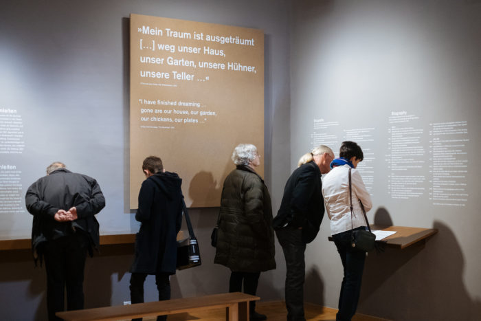 Fünf Personen lesen einen Ausstellungstext an einer Wand und erkunden den großen Bruch in einer Galerie.