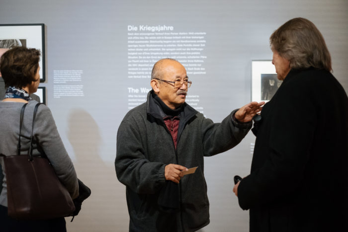 Drei Personen diskutieren vor musealen Texttafeln über einen großen Bruch in der Geschichte.