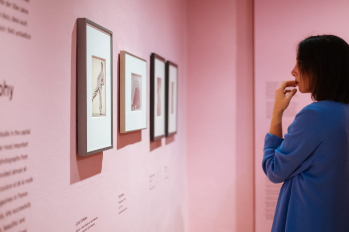 Eine Person betrachtet gerahmte Fotografien aus Der große Bruch in einer Kunstgalerie mit rosa Wänden.