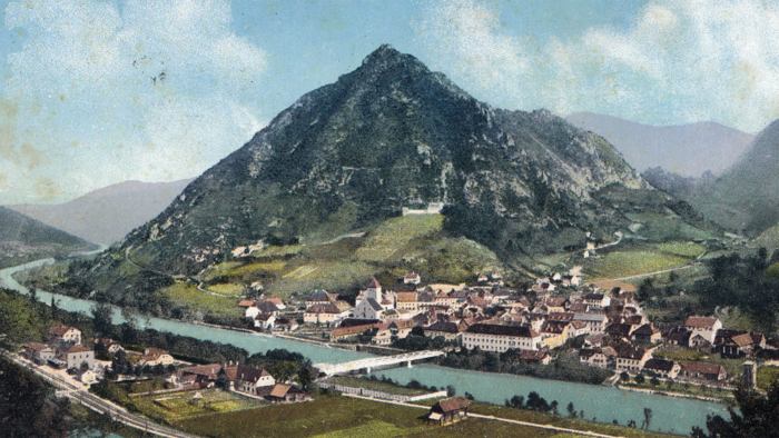Eine kleine Stadt mit einem Fluss liegt am Fuße eines steilen, grünen Berges.