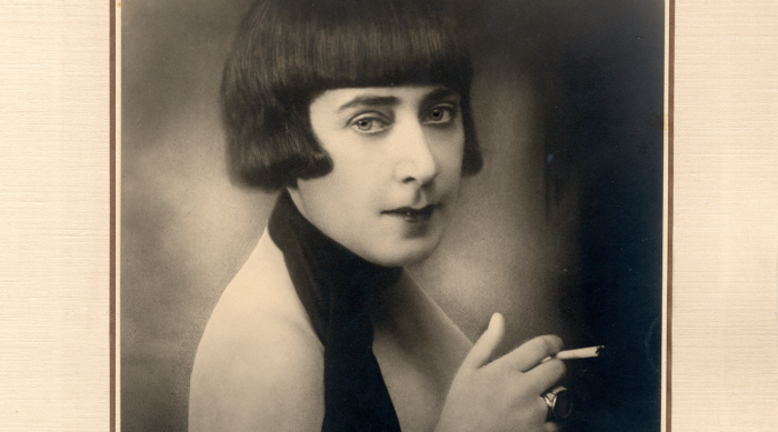 Schwarz-weißes Porträt einer Die Neue Frau mit kurzen Haaren, die eine Zigarette hält und in die Kamera schaut.