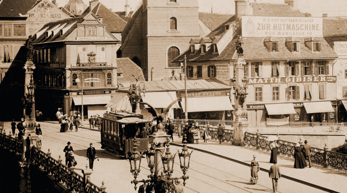 Historische Straßenszene mit einer Straßenbahn, Fußgängern und Boulevards in einer europäischen Stadt.