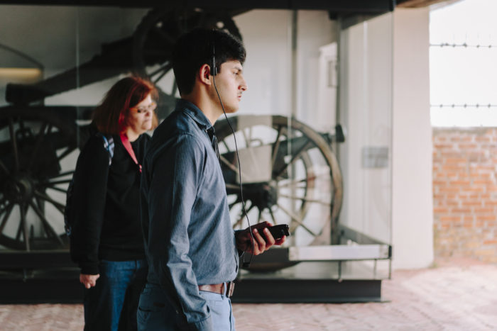 Ein Mann und eine Frau stehen in der Kanonenhalle und blicken auf die Stadt Graz, im Hintergrund sind historische Kanonen hinter einer Glaswand zu sehen.