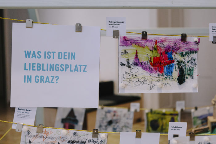 Ein Schild in deutscher Sprache fragt nach Lieblingsausflügen in Graz, neben den bunten Zeichnungen der Kinder.