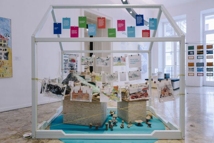 Kunstausstellung in Graz zeigt Kinder-Skizzen, Bilder und Notizen in einer hausförmigen Rahmenkonstruktion.