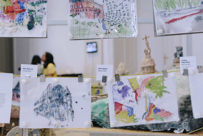 Kinder zeigen bunte Zeichnungen auf einer Leine in einer Ausstellung in Graz.