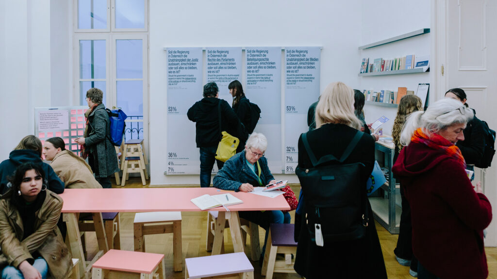 In einem modernen, hell erleuchteten Lesesaal zum Thema Demokratie werden Bücher und Schautafeln betrachtet.