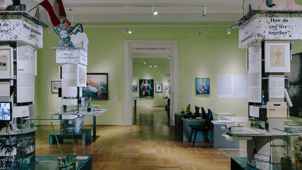 Kunstausstellung in Graz mit Werken aus den Jahren 1945-1965 mit Tafeln, gerahmter Kunst und Vitrinen.
