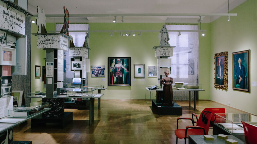 Ausstellungsraum des Museums in Graz mit Gemälden, Vitrinen und Tafeln an grünen Wänden.