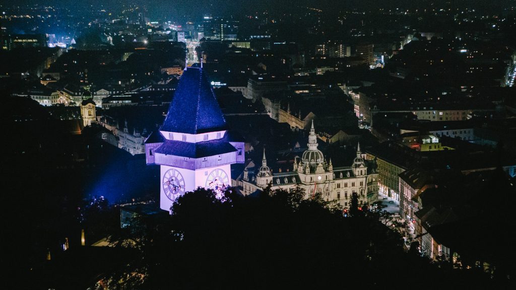 Nachtansicht des Schlossbergs mit seinem beleuchteten Uhrenturm, in der Nähe des Langer Samstag des Graz Museums.
