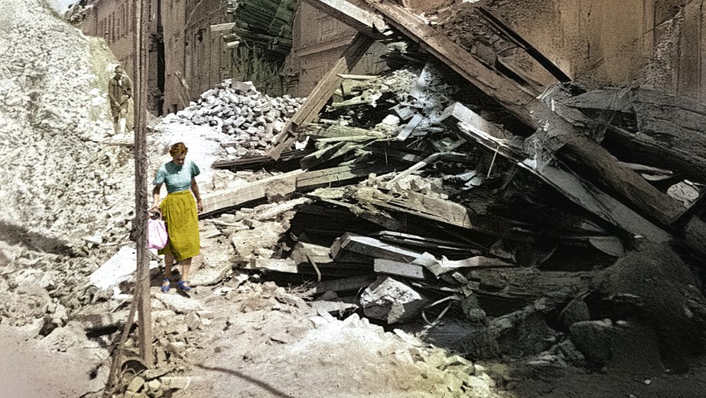 Eine Frau und ein Kind gehen an Trümmern in Graz 1945-1965 vorbei und erinnern an Ins Ungewisse.