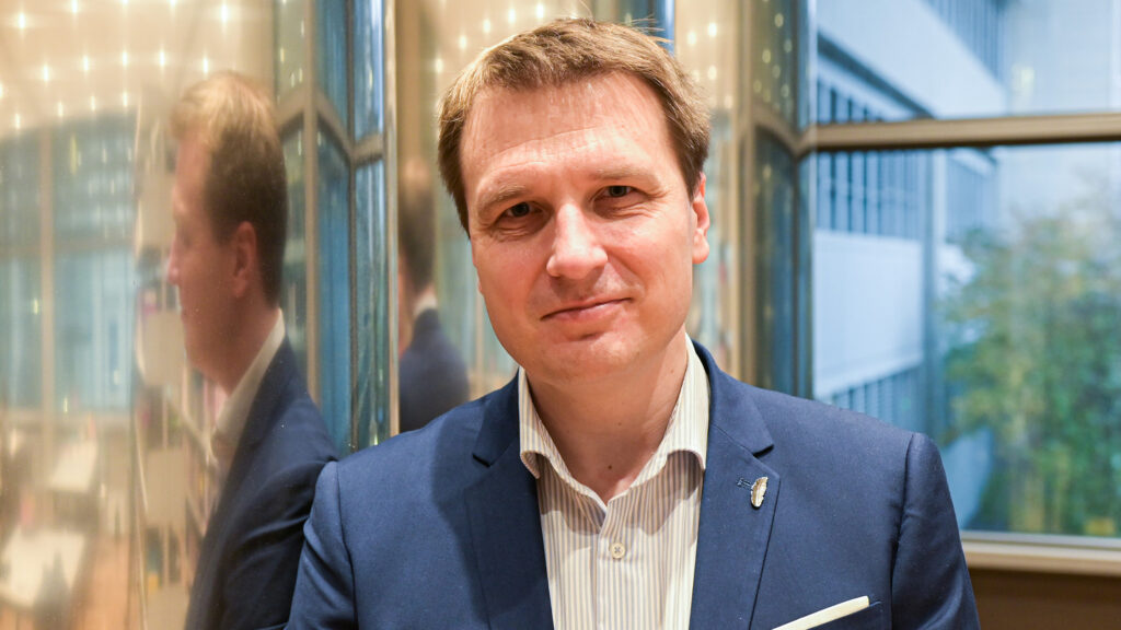 Ein Mann in einem blauen Anzug steht drinnen vor reflektierenden Wänden und träumt von Georgien.