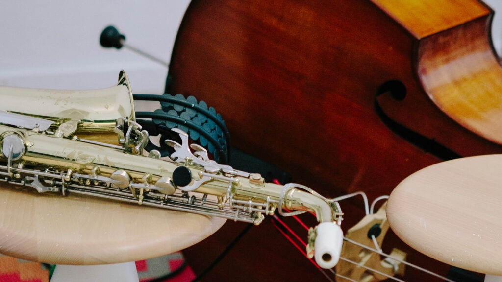 Ein Saxophon und ein Kontrabass stehen auf Hockern in einem Musikübungsraum.