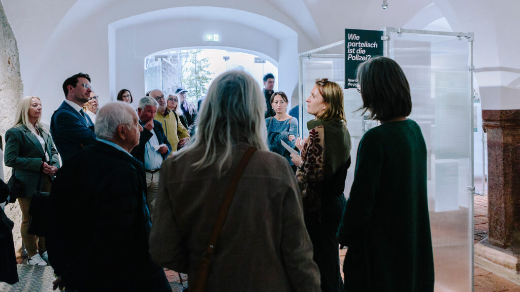 Eine Gruppe von Freund*innen hört einer Frau zu, die in einem Ausstellungsraum des Graz Museums spricht.