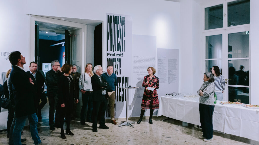 Eine Gruppe hört einer Frau zu, die bei der Ausstellung Protest! im Galerieraum des Graz Museums spricht.