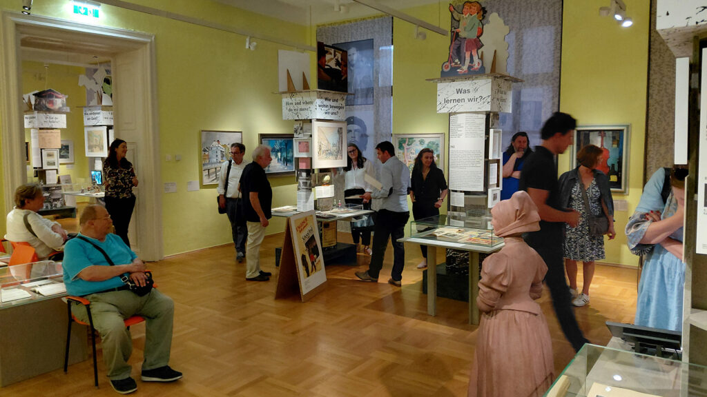 In einem gut beleuchteten Raum des Graz Museums mit elegantem Holzfußboden werden Exponate betrachtet.