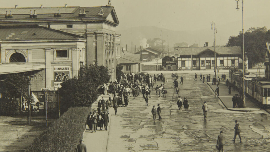 Schwarz-Weiß-Foto von Menschen an großen Gebäuden in der Nähe des Bahnhofs Koralmbahn.
