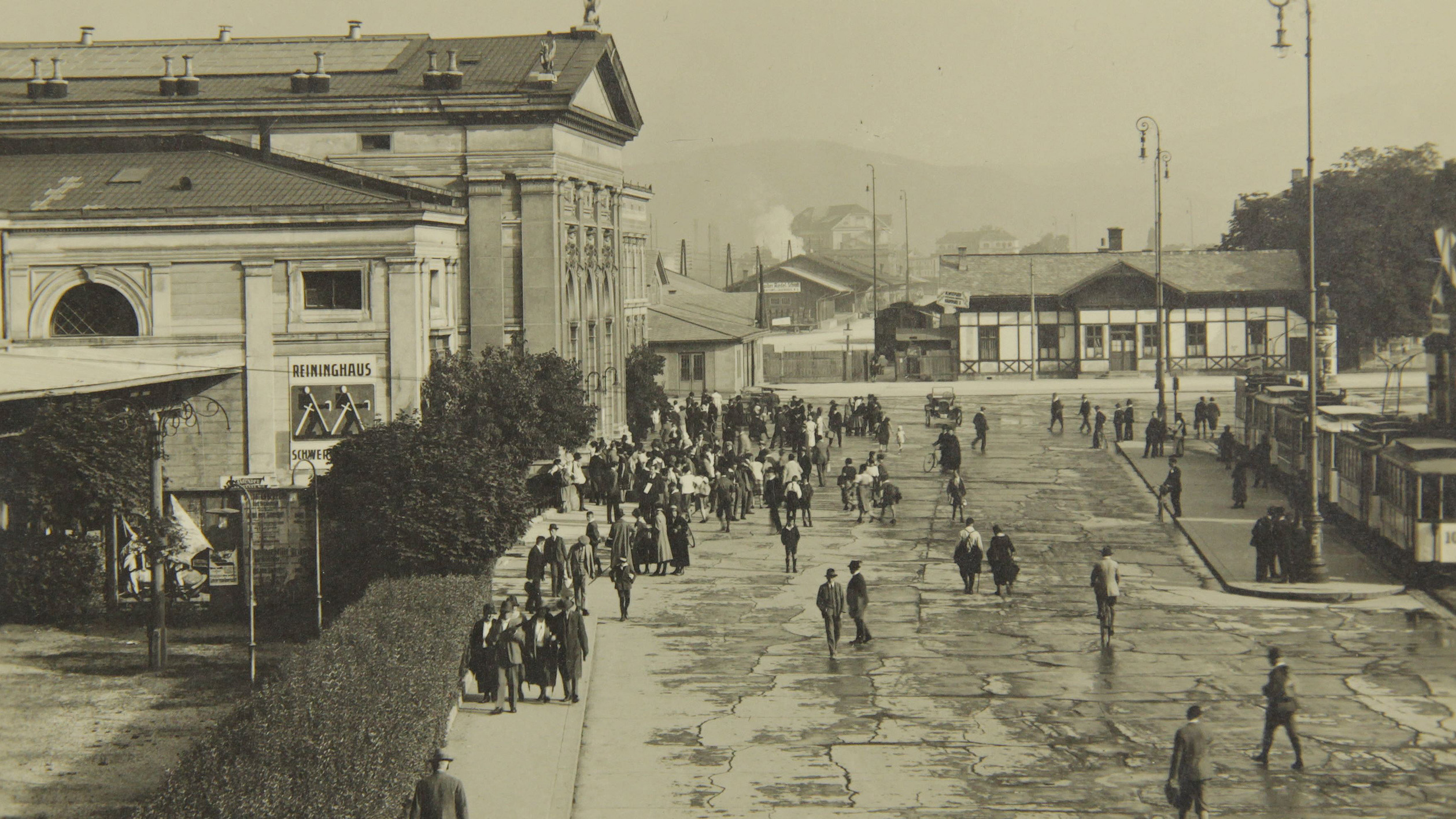 Schwarz-Weiß-Foto von Menschen an großen Gebäuden in der Nähe des Bahnhofs Koralmbahn.