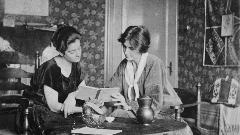 Zwei Frauen lesen in einem alten, gemusterten Raum über vertriebene Komponistinnen.