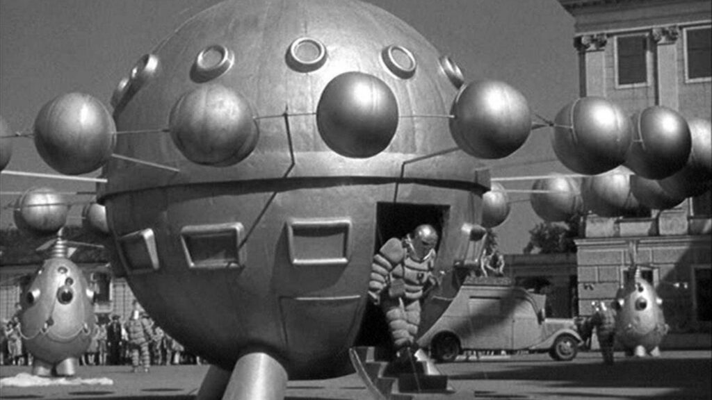 Im April 2000 verlässt eine Person in einem Raumanzug ein kugelförmiges Raumschiff inmitten schwebender Stadtkugeln.