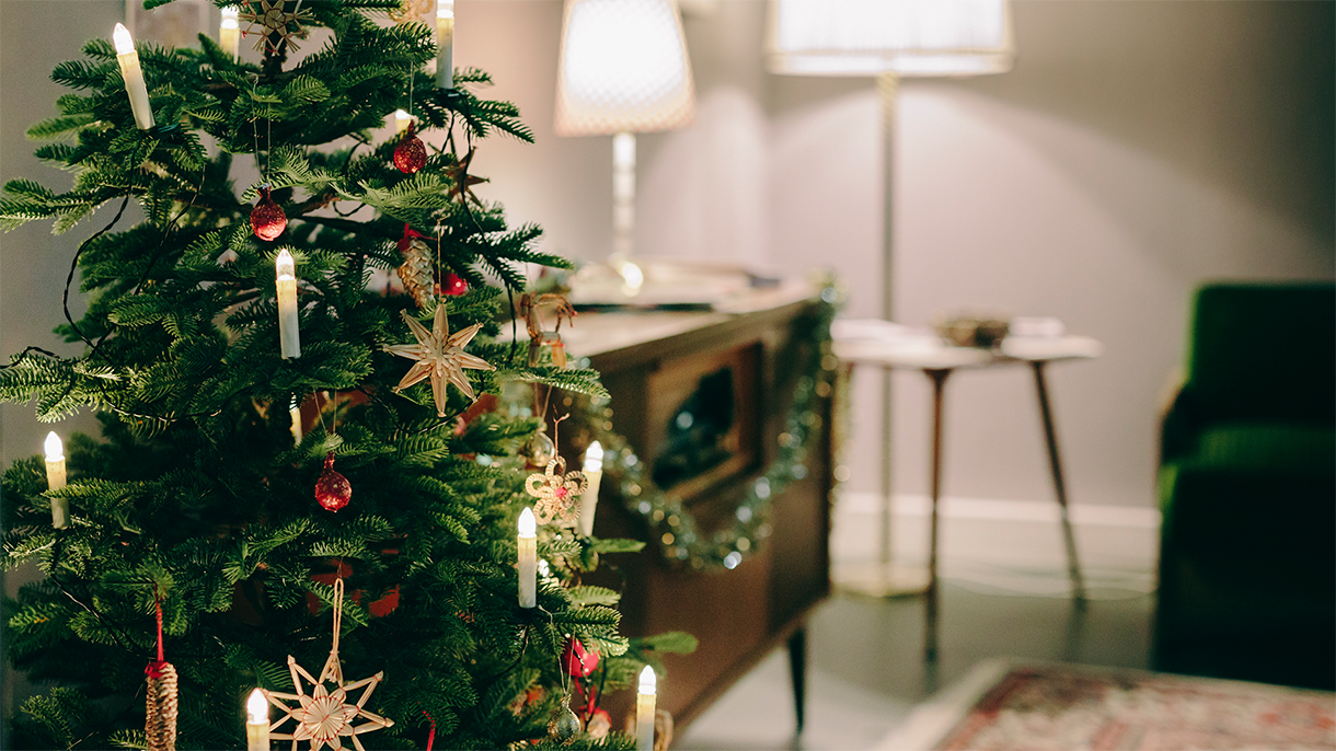Ein geschmückter Weihnachtsbaum mit Lichtern und Ornamenten in einer gemütlichen Wohnzimmerumgebung.