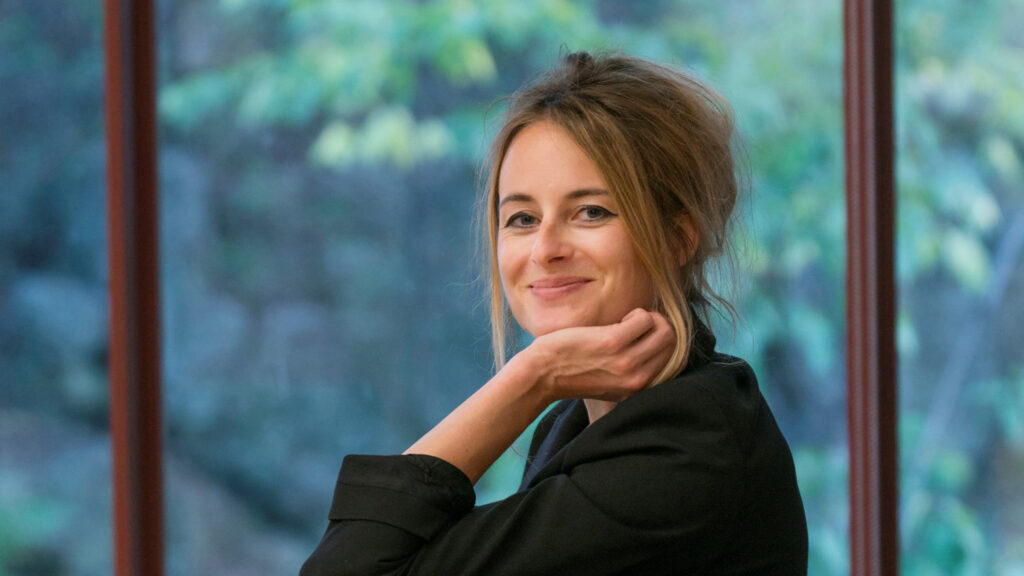 Eine Frau mit zurückgebundenem Haar in einer schwarzen Jacke, die lächelnd drinnen-nie mehr weinen.