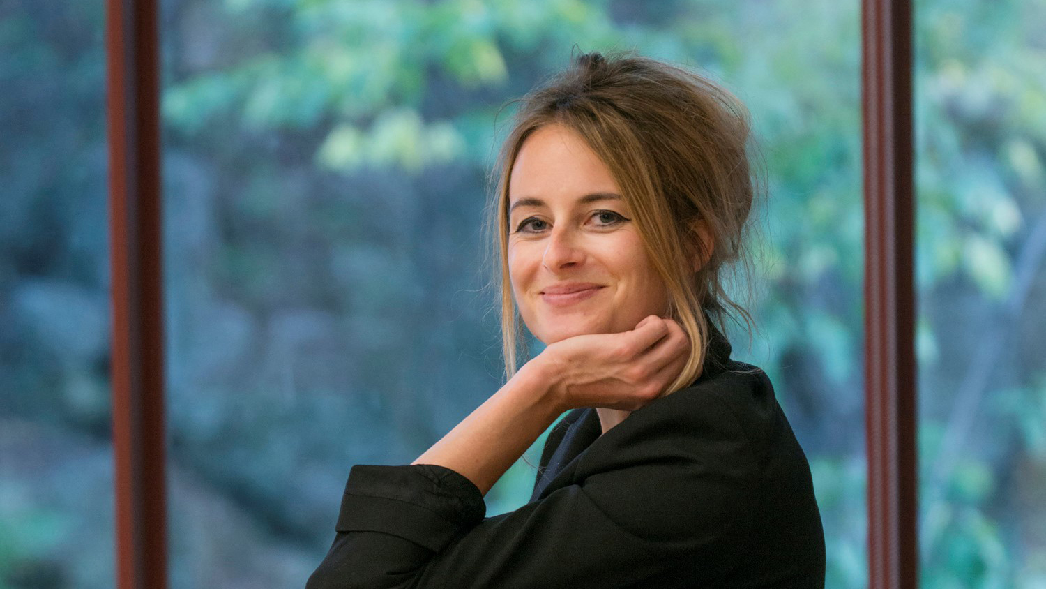 Eine Frau mit zurückgebundenem Haar in einer schwarzen Jacke, die lächelnd drinnen-nie mehr weinen.