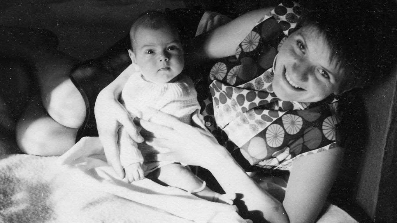 Eine Frau der Schattengeneration lächelt in die Kamera und hält ein Baby auf dem Schoß.