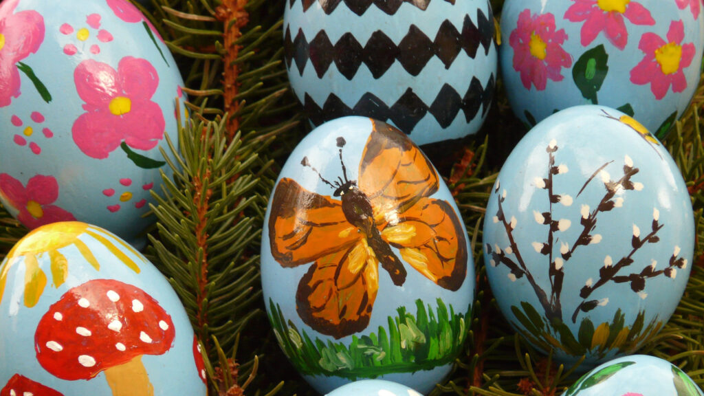 Blaues Demokratie-Ei mit bunten Blumen, Schmetterlingen, Pilzen und Baumzweigen verziert.