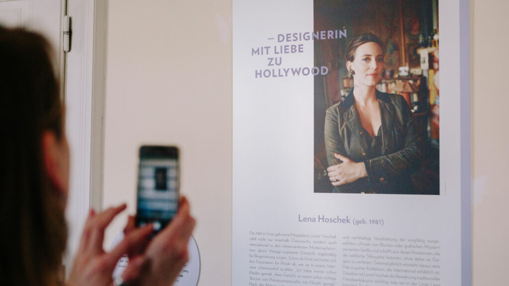 Eine Person knipst ein Foto von Lena Hoscheks Plakat in der Pionierinnengalerie im Rathaus.
