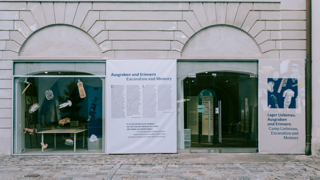 Museumseingang mit Bannern zu den Ausstellungen „Lager Liebenau: Erinnern“ und „Ausgraben“.