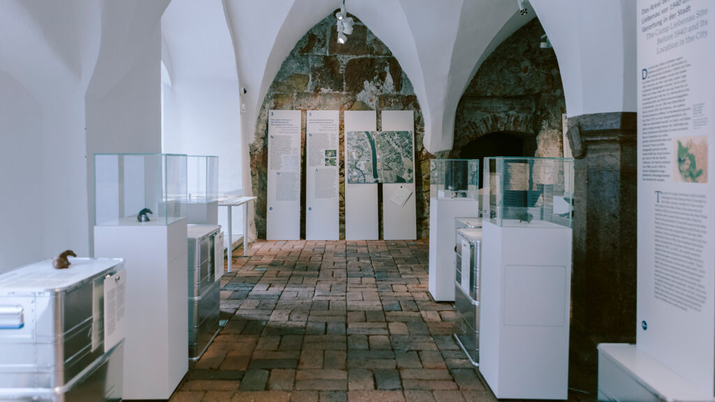 Ausstellungsraum des Museums, der an das Lager Liebenau erinnert, mit Vitrinen, Schautafeln und Ziegelboden.