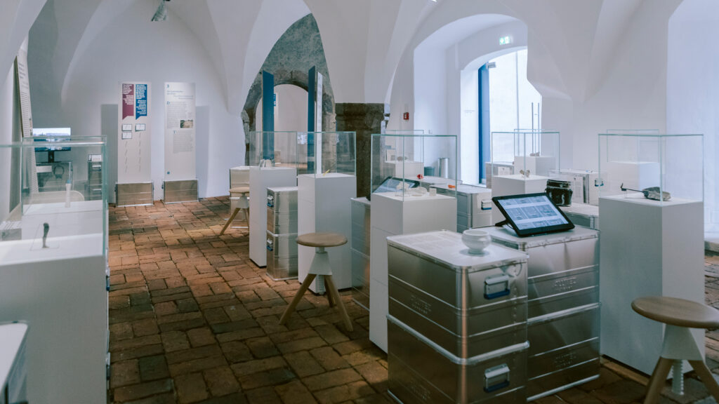 Diese moderne Museumsausstellung erinnert mit Glasvitrinen, Hockern und digitalen Displays an das Lager Liebenau.