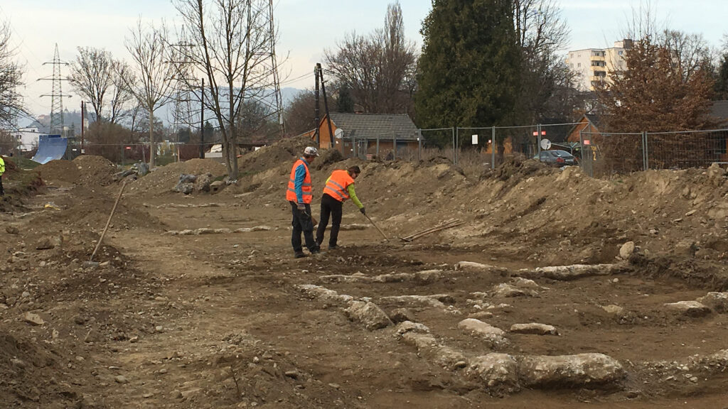 Zwei Arbeiter in Sicherheitswesten untersuchen Spuren in der ehemaligen archäologischen Ausgrabungsstätte Lager Liebenau.