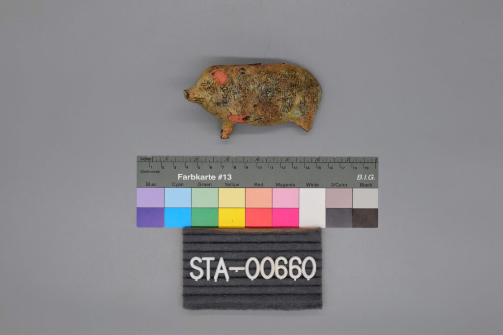Kleine Schweinefigur über einer Farbskala und einem Etikett mit der Aufschrift STA-00660 auf grauem Hintergrund.