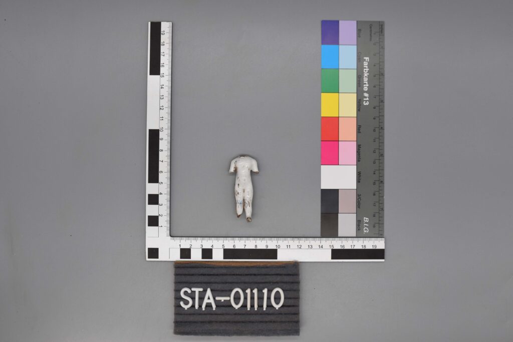 Eine kleine, arm- und beinlose Figur wird neben Mess- und Farbskalen aufgestellt.