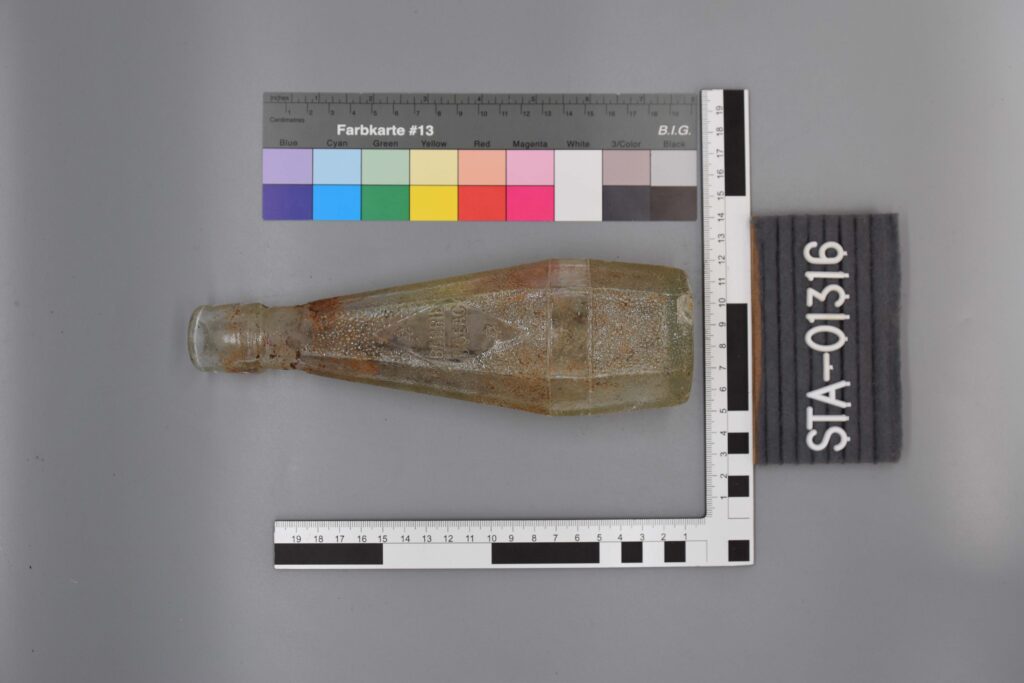 Alte, leere Glasflasche mit Schmutz darin, die neben Mess- und Farbskalen steht.