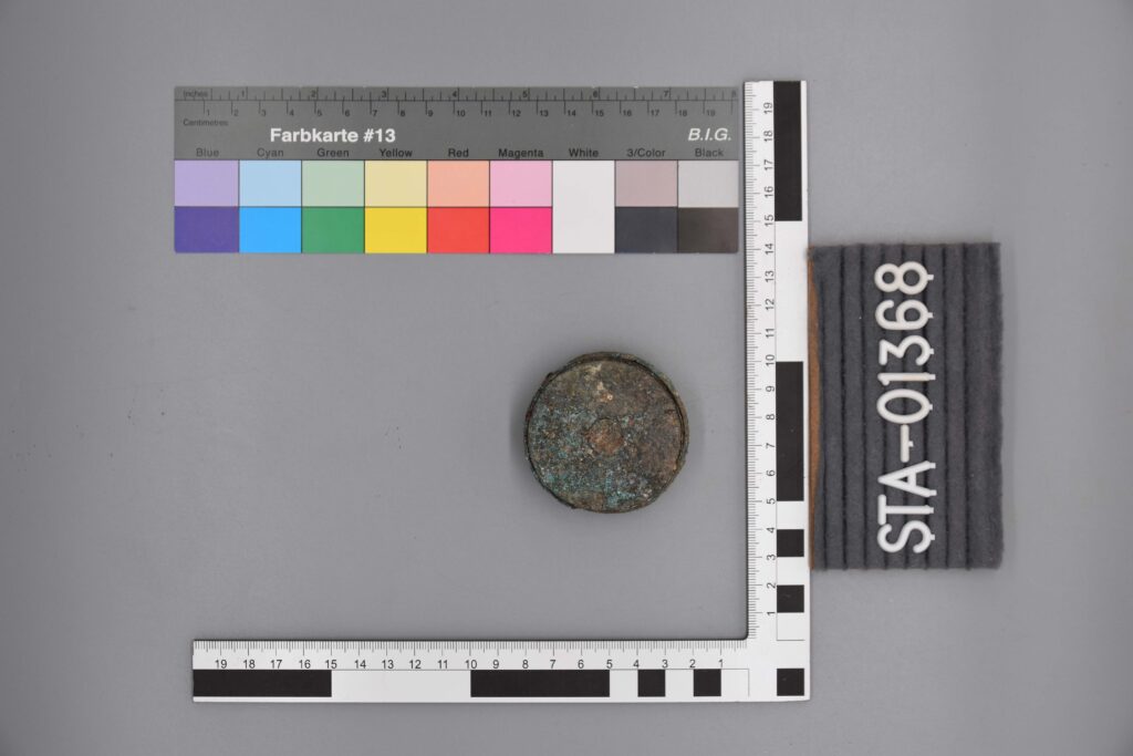 Eine korrodierte Metallscheibe neben den Farb- und Messskalen mit der Aufschrift STA-01368.