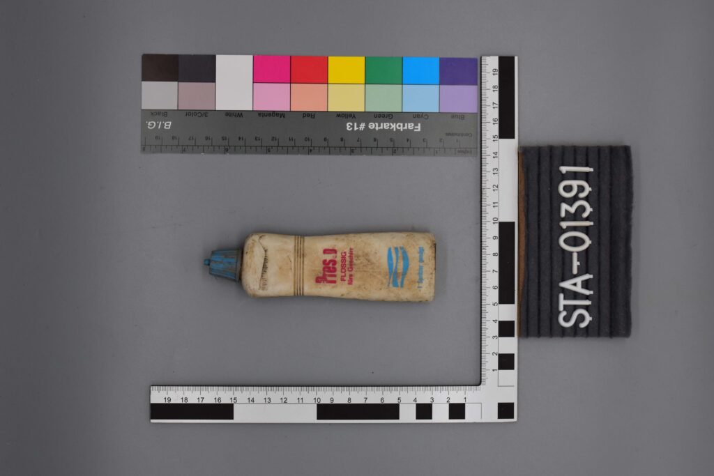 Weiße Flasche mit blauem Deckel, mit Linealen gemessen, mit der Aufschrift STA-01391 auf einem schwarzen Etikett.