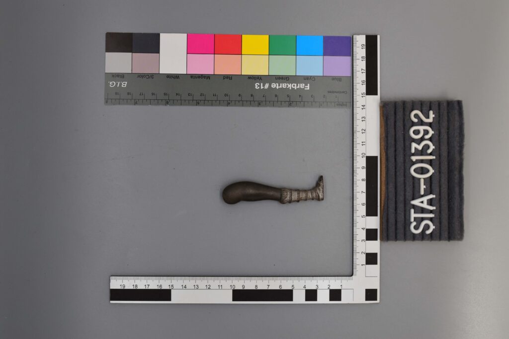 Kleine, dunkle Griff-Ausstellungsobjekte zwischen Farb- und Messskalen; beschriftet mit STA-01392.