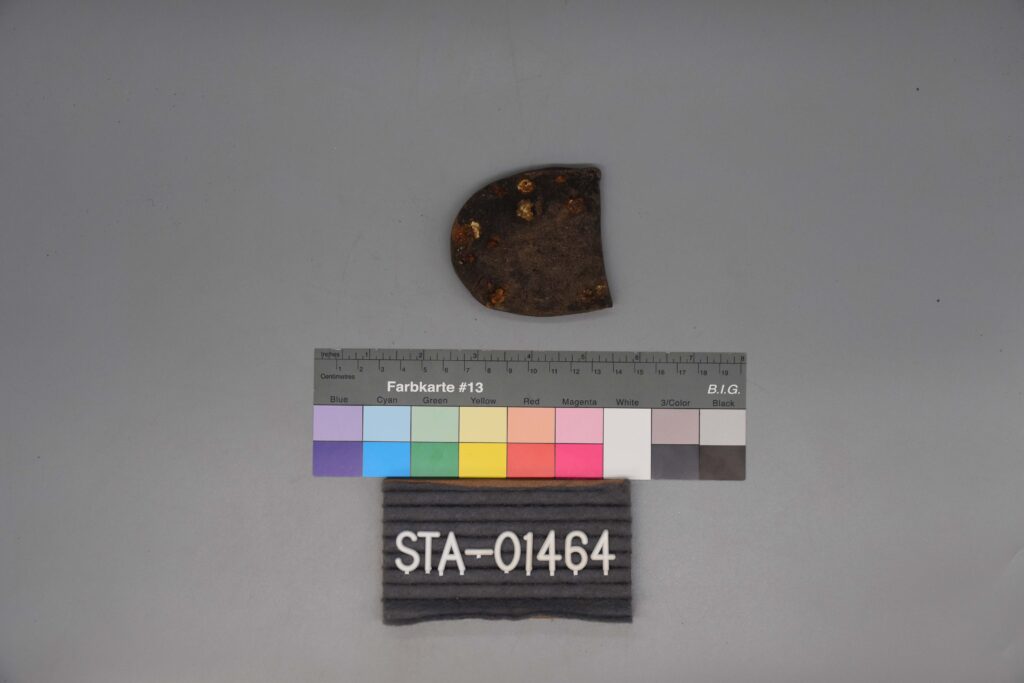Halbkreisförmiges Metall-Artefakt über einer Farbskala und einem Etikett mit der Aufschrift STA-01464.