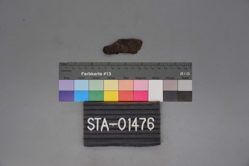 Ein kleines verrostetes Metallobjekt über einer Farbskala mit der Aufschrift STA-01476.