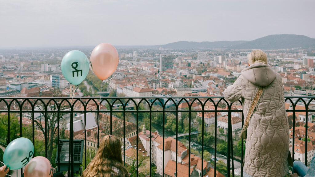Menschen mit Luftballons genießen den Blick auf die Stadt vom hohen Aussichtspunkt des Schlossbergs.