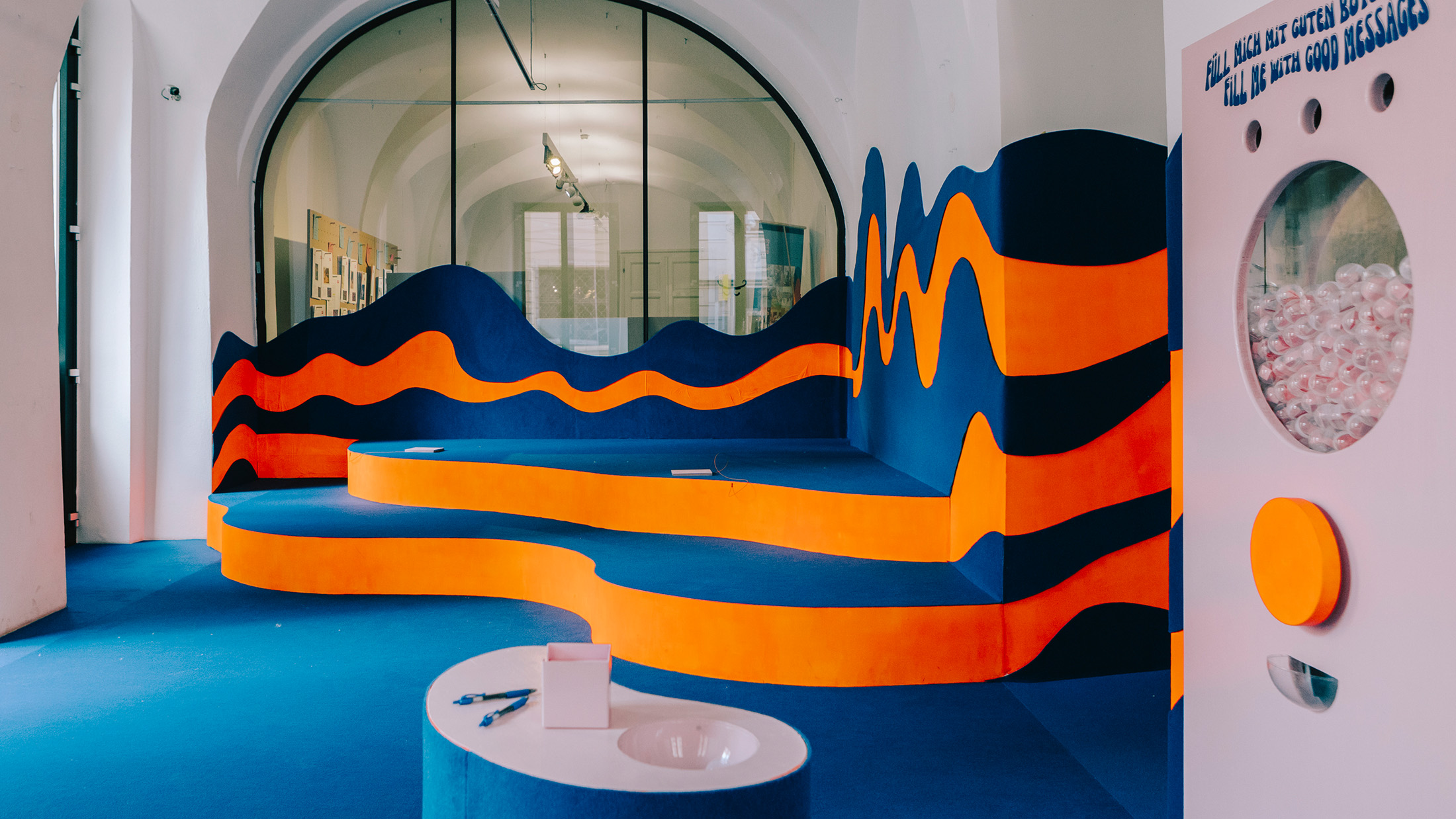 Modernes Interieur mit von Flux inspirierten, wellenförmigen Sitzgelegenheiten, geschwungenen Wänden und einem weißen interaktiven Display.