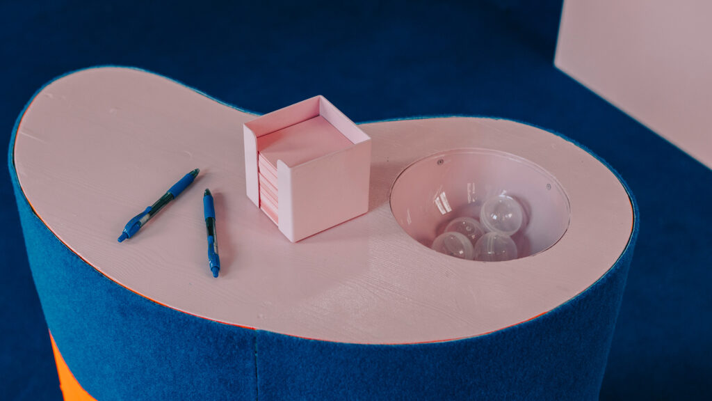 Zwei Stifte, eine rosa Schachtel und durchsichtige Flux-Kunststoffkugeln auf einem nierenförmigen Tisch mit blauer Einfassung.