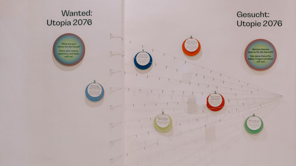 Wall display with ‘70s in Graz-style Utopia 2076 signs in English and German, with empty holders.