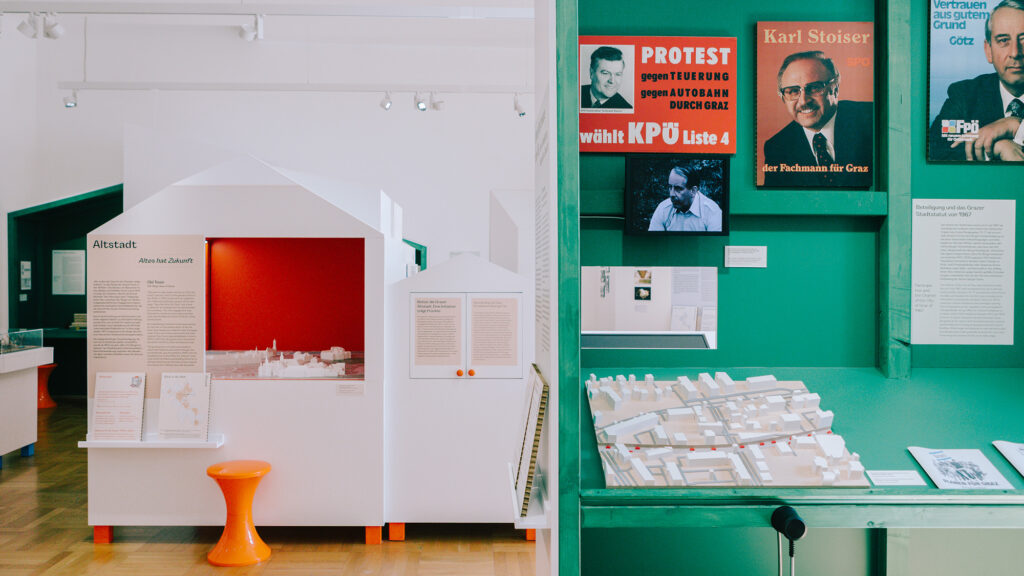 Museum exhibit featuring architectural models, 70s in Graz history, and political posters.