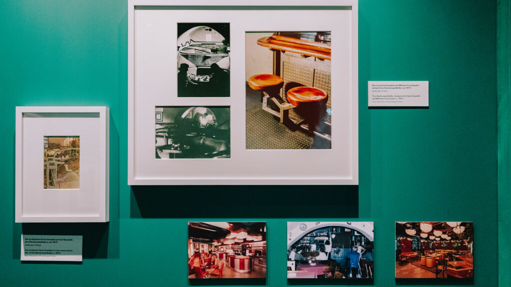 Framed photos of 70s in Graz diner interiors and stools displayed on a green wall.